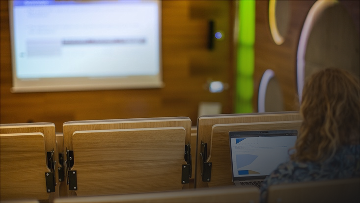 Frau vor Laptop in einem Vorlesungssaal