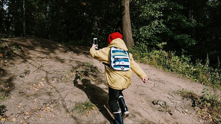 Mann in der braunen Jacke und Hose, der ein schwarze Smartphone hält