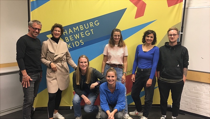 Eine Gruppe vor einem Plakat, bestehend aus Männern und Frauen